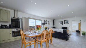 A modern kitchen with a dining area, a sofa, and a TV. - Cosy Aberdeenshire Stone Cottage (Caernarfon)