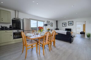 A modern kitchen with a dining area, a sofa, and a TV. - Cosy Aberdeenshire Stone Cottage (Caernarfon)