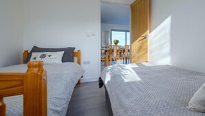 A bedroom with two beds, a wooden door, and a view of a dining area. - Cosy Aberdeenshire Stone Cottage (Caernarfon)