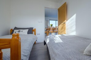 A bedroom with two beds, a wooden door, and a view of a dining area. - Cosy Aberdeenshire Stone Cottage (Caernarfon)