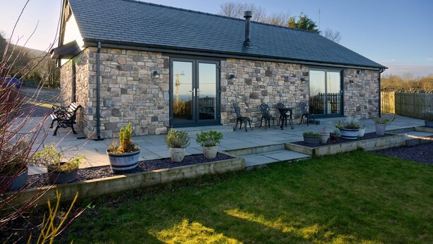 A stone building with a large glass door, outdoor seating, and a garden with potted plants. - Cosy Aberdeenshire Stone Cottage (Caernarfon)