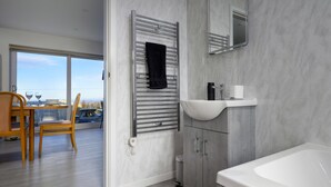 A modern bathroom with a bathtub, a sink, and a towel rack. - Cosy Aberdeenshire Stone Cottage (Caernarfon)