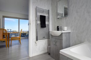 A modern bathroom with a bathtub, a sink, and a towel rack. - Cosy Aberdeenshire Stone Cottage (Caernarfon)