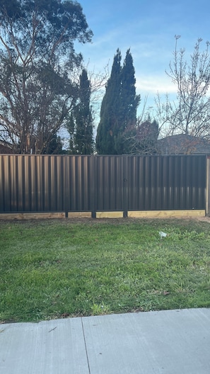 A fenced yard with a grassy area and trees in the background. - Donvale holiday home  relaxing .15 minutes drive to CBD one minute walk to bus s (Donvale)