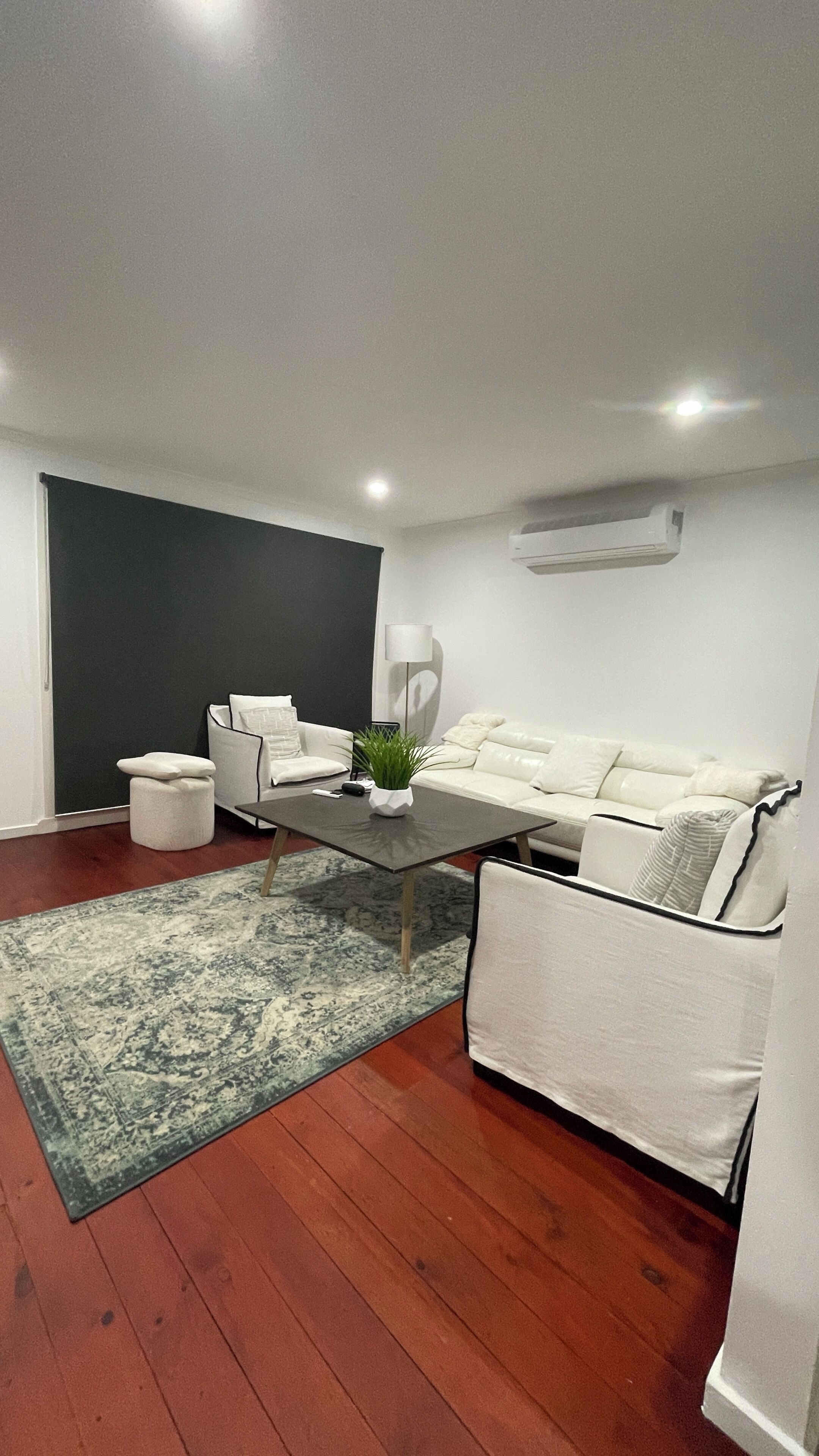 A modern living room with a white sofa, a coffee table, a small white ottoman, and a patterned rug.