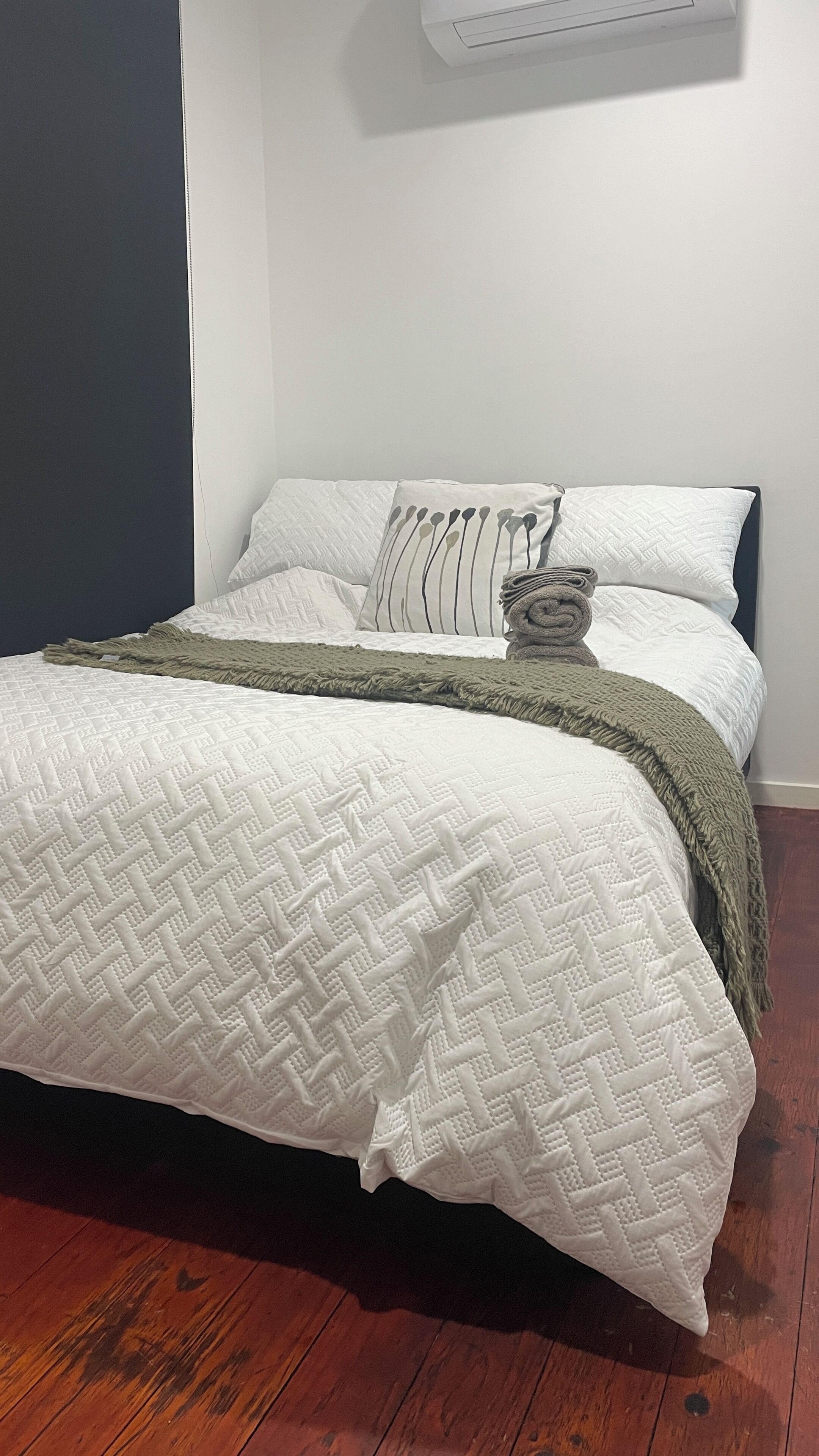 A bed with a white quilt, a green throw blanket, and a rolled-up blanket.