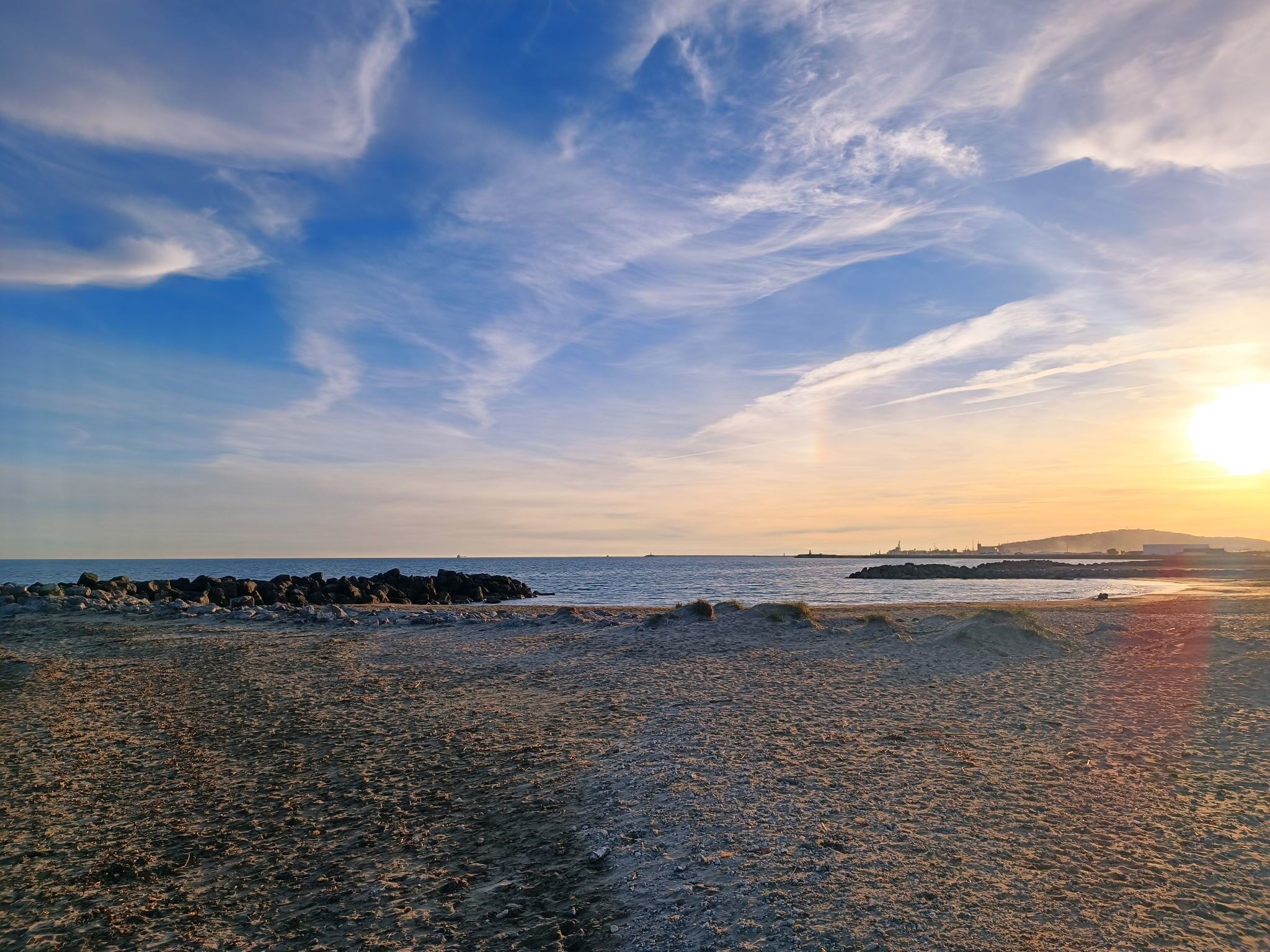 Uma praia com costa rochosa, ondas e um pôr do sol.