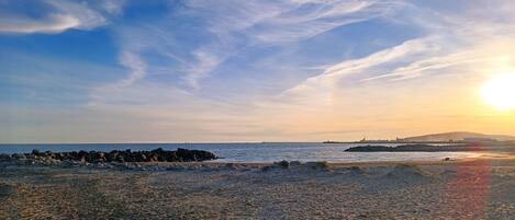 Une plage avec un rivage rocheux, des vagues et un coucher de soleil.