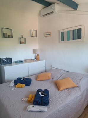 Ein ordentlich bezogenes Bett mit einer grauen, strukturierten Bettdecke, zwei orangen Kissen und aufgerollten Handtüchern.