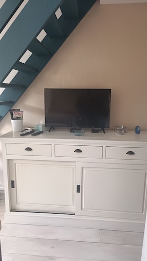 A white entertainment unit with a flat-screen TV, remote controls, and a cup with magazines. - Beautiful 2-Bedroom Townhouse, Frontignan, Secure Residential Complex, Beach Access 100 m Away (Frontignan)