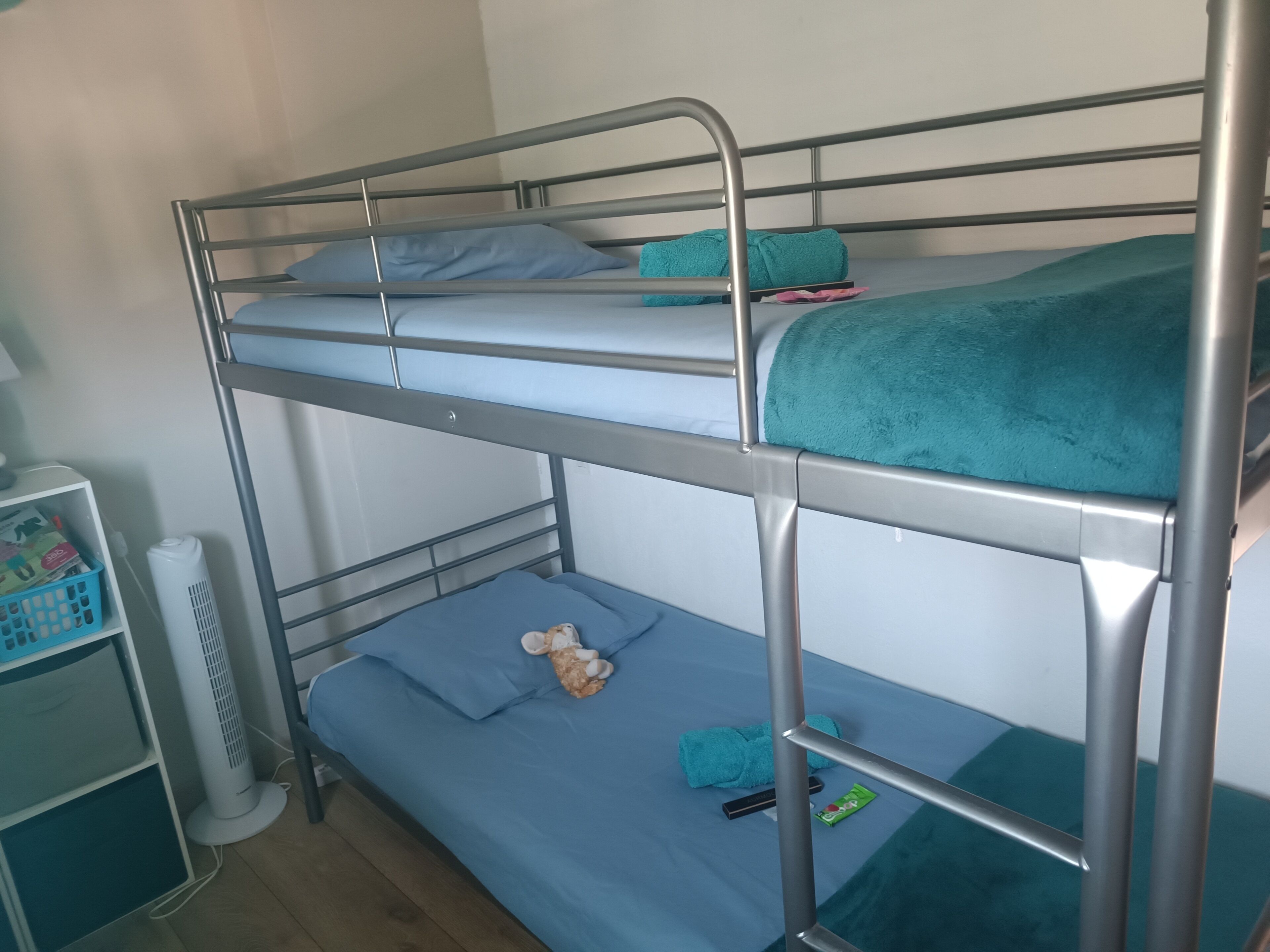 A bunk bed with a white fan and a small shelf unit.