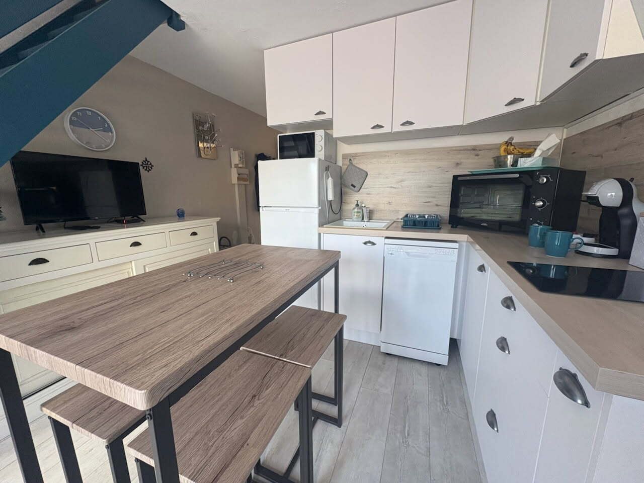 Uma cozinha compacta com mesa de jantar, armários brancos, micro-ondas e lava-louças.