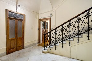 A hallway with a wooden door, a staircase with a wrought iron railing, and a tiled floor. - La Dimora Dei Reali - Grey Suite with Balcony, Wi-Fi and Air Conditioning (Naples)