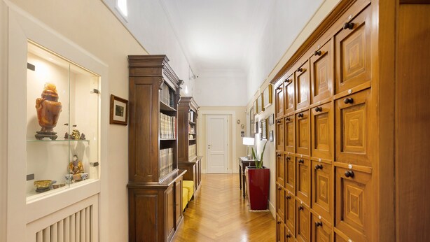 Un pasillo con armarios de madera, una vitrina de vidrio con objetos decorativos y una maceta roja.