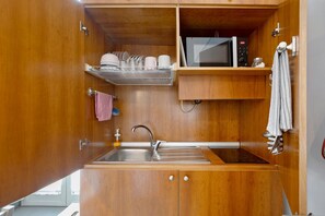A compact kitchen with a sink, a microwave, and a shelf with dishes. - La Dimora Dei Reali - Grey Suite with Balcony, Wi-Fi and Air Conditioning (Naples)