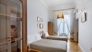 Habitación de hotel con dos camas, un armario, una mesita de noche, una lámpara y una ventana con cortinas.