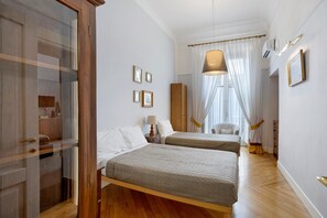 Ein Hotelzimmer mit zwei Betten, einem Kleiderschrank, einem Nachttisch, einer Lampe und einem Fenster mit Vorhängen.