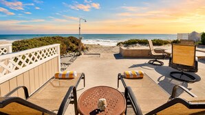 A beachside patio with a table and chairs, a wooden deck, and a view of the ocean.