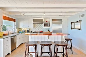 A modern kitchen with white cabinetry, a central island with stools, a microwave, and a refrigerator.