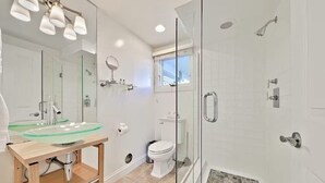 A modern bathroom with a glass shower enclosure, a glass sink, and a toilet.