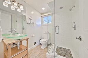 A modern bathroom with a glass shower enclosure, a glass sink, and a toilet.
