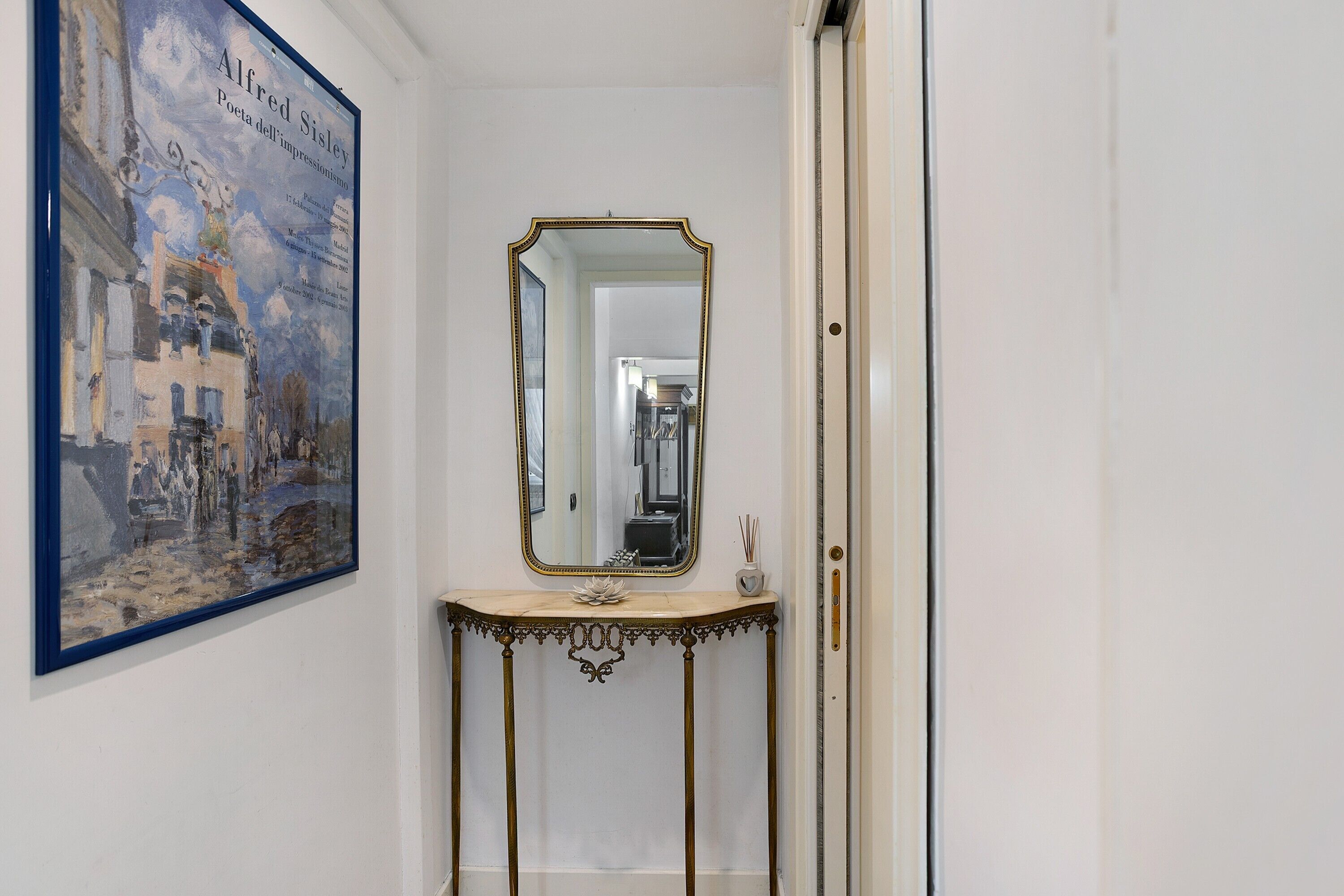 Un couloir orné d’un tableau encadré, d’un miroir et d’une console sur laquelle est posé un vase.