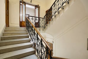 A staircase with a wooden handrail and black metal balusters, leading to a door with a glass panel. - La Dimora Dei Reali – Yellow Suite with Wi-Fi and Air Conditioning (Naples)