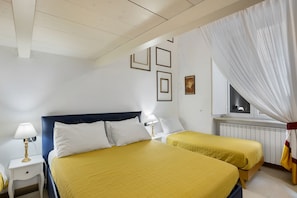Une chambre d’hôtel avec deux lits, une table de chevet, une lampe, une fenêtre avec des rideaux et des tableaux encadrés au mur.