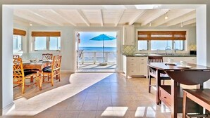 A spacious kitchen with a view of the sea, a dining area with wooden chairs, and a large window with a blue umbrella. - On The Sand, Perfect 4 Families, Endless Sunset Views! (Dana Point)