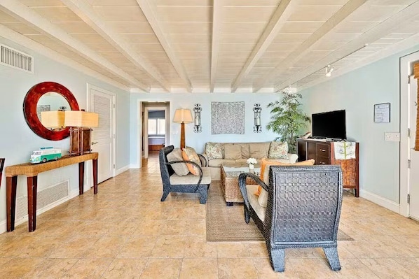A spacious living area with a high ceiling, a sofa set, a television, and a console table with a lamp.