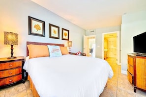 A hotel room with a large bed, two bedside tables with lamps, a television, and framed pictures on the wall.