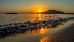Une plage avec des vagues au coucher du soleil, un ciel dégagé et une montagne lointaine.