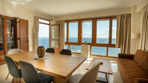 A dining area with a wooden table, chairs, a vase, and a view of the sea through large windows. - Villa 'Vignetta Mare 2br Seaview Retreat' with Sea View, Wi-Fi and Air Conditioning (Ermoupoli)