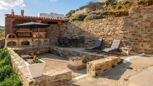 Une terrasse en pierre avec coin salon extérieur, un espace barbecue et une vue sur le paysage environnant.