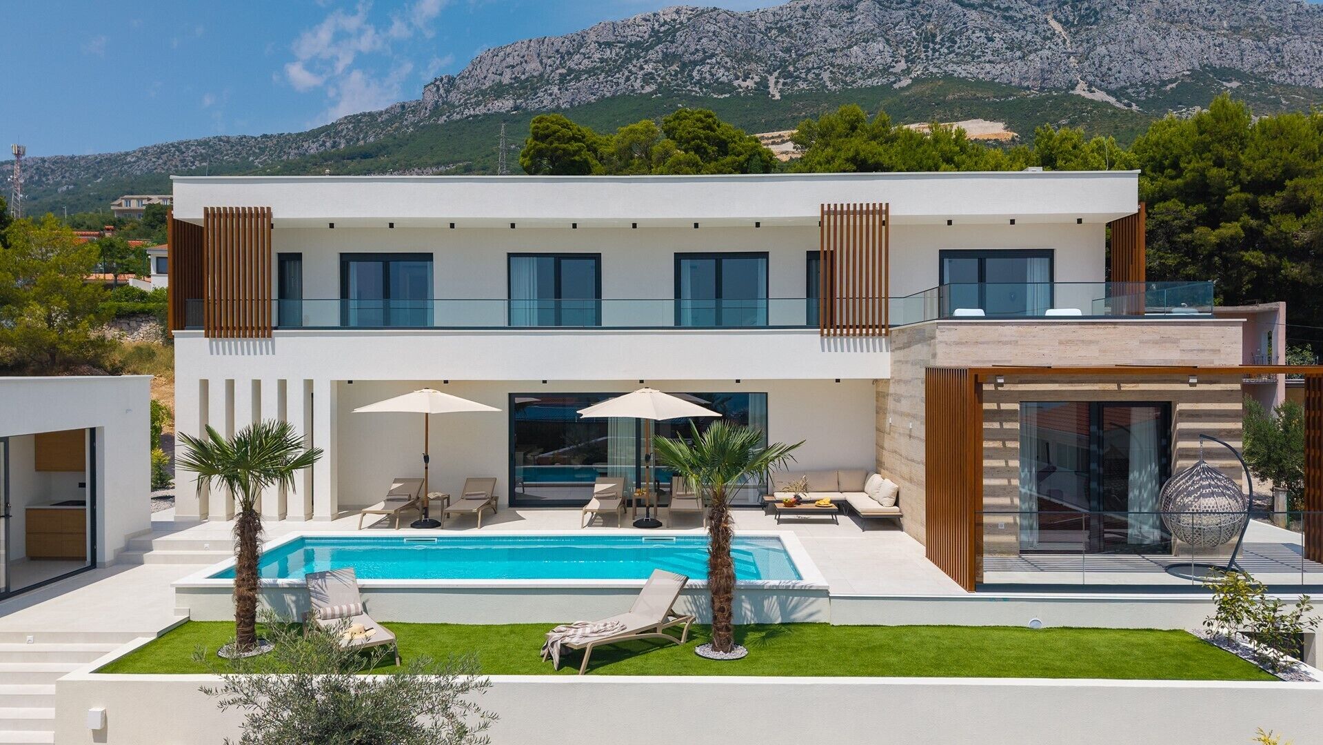 A modern two-story house with a swimming pool, outdoor seating, and a mountain backdrop.