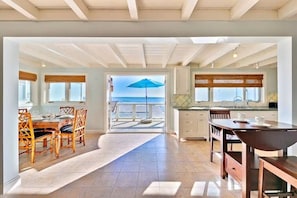 Una cocina amplia con vista al mar, un comedor con sillas de madera y un ventanal con un paraguas azul.