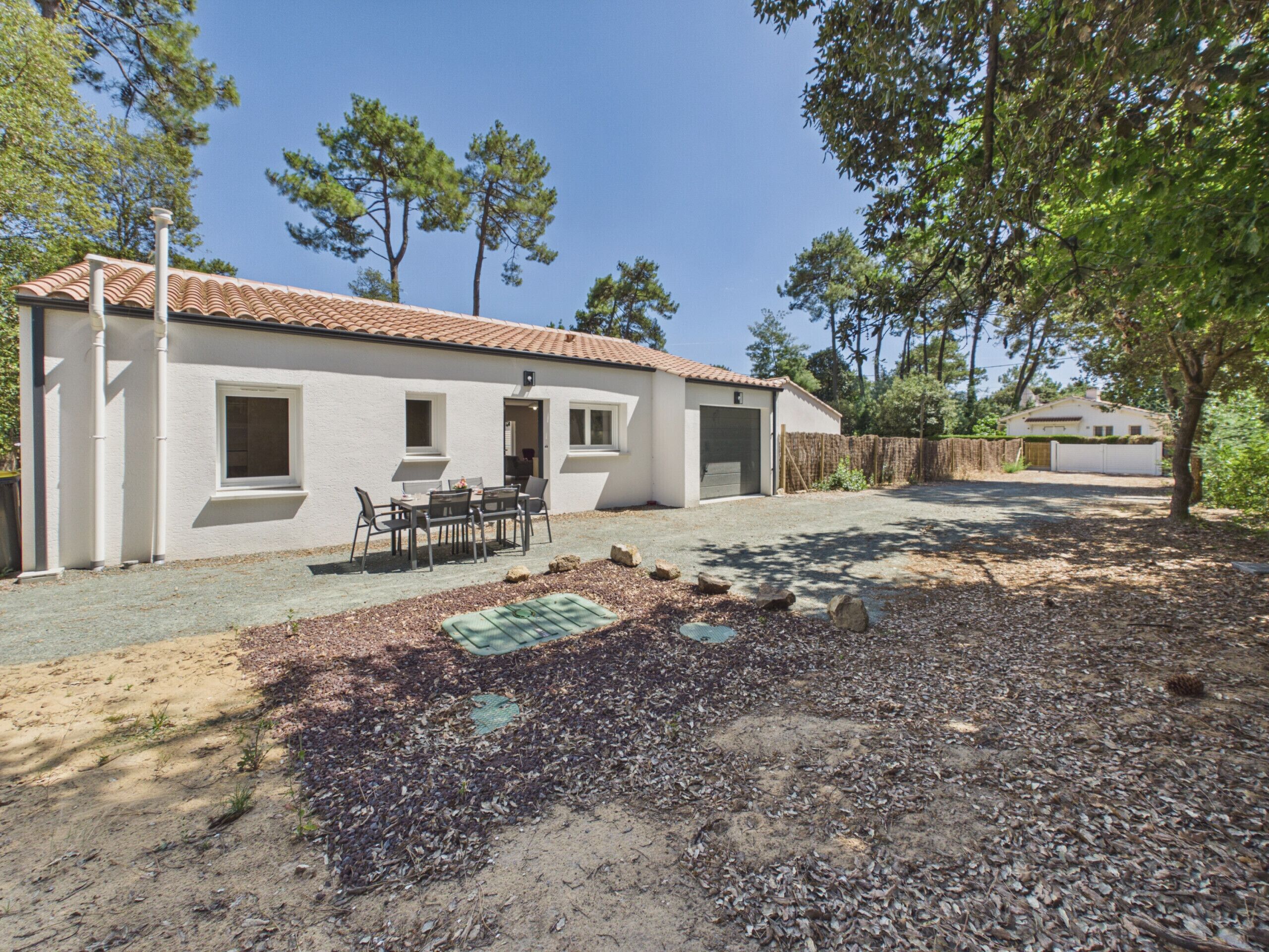 A single-story building with a tiled roof, a covered patio area with a table and chairs, and a gravel driveway.