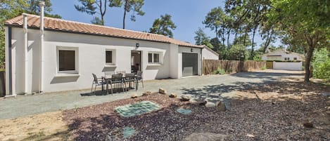 A single-story building with a tiled roof, a covered patio area with a table and chairs, and a gravel driveway.