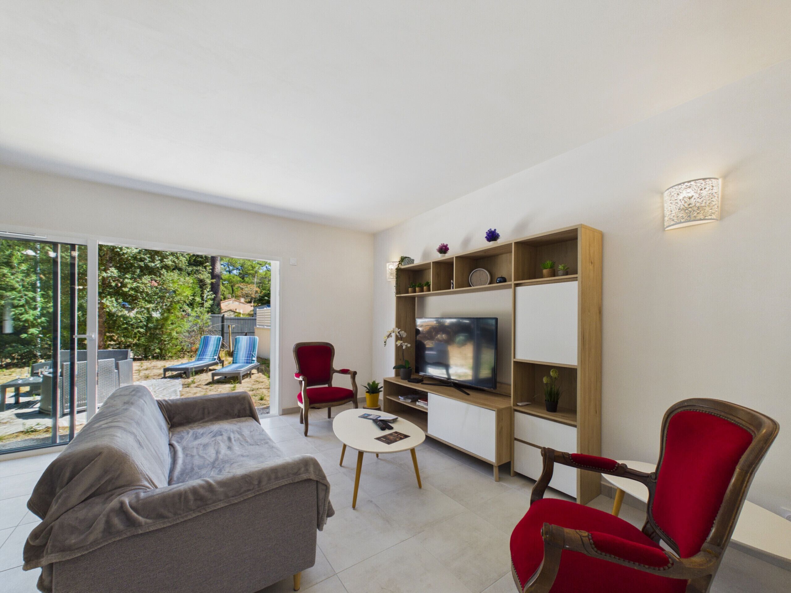 A modern living room with a sofa, red chairs, a TV, and a bookshelf.