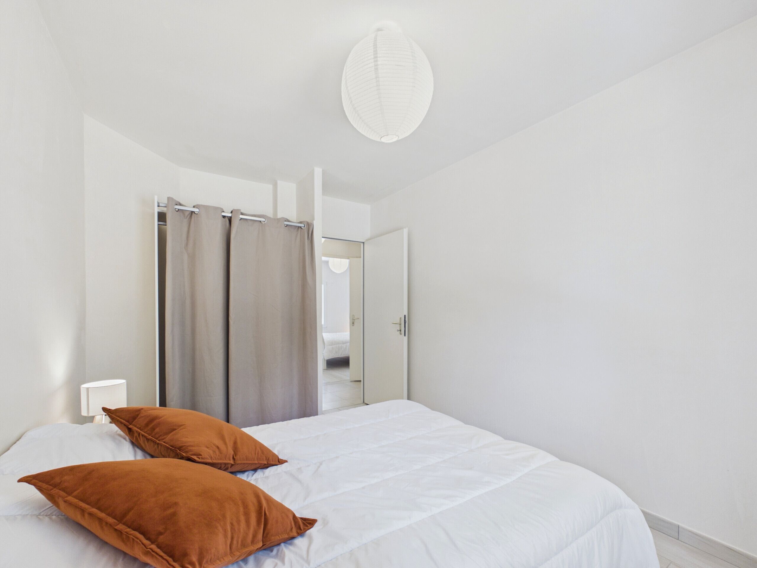 Une chambre à coucher avec un lit, deux oreillers, un rideau, une porte et un luminaire.