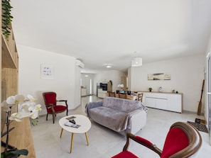 Un grand espace de vie comprenant un canapé, des fauteuils, une petite table et une cuisine à l’arrière-plan.