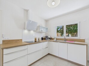 A modern kitchen with white cabinets, a wooden countertop, a built-in microwave, and a window with a view of greenery.
