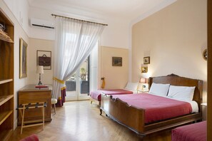 Hotellihuone, jossa on puinen sänky, kaksi yöpöytää, työpöytä, tuoli, ikkuna, jossa on ohuet verhot, ja näkymä ulos.