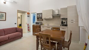 Een knus woongedeelte met een kitchenette, een zithoek met een houten tafel en stoelen, een bank en een deur naar een badkamer met een douche.