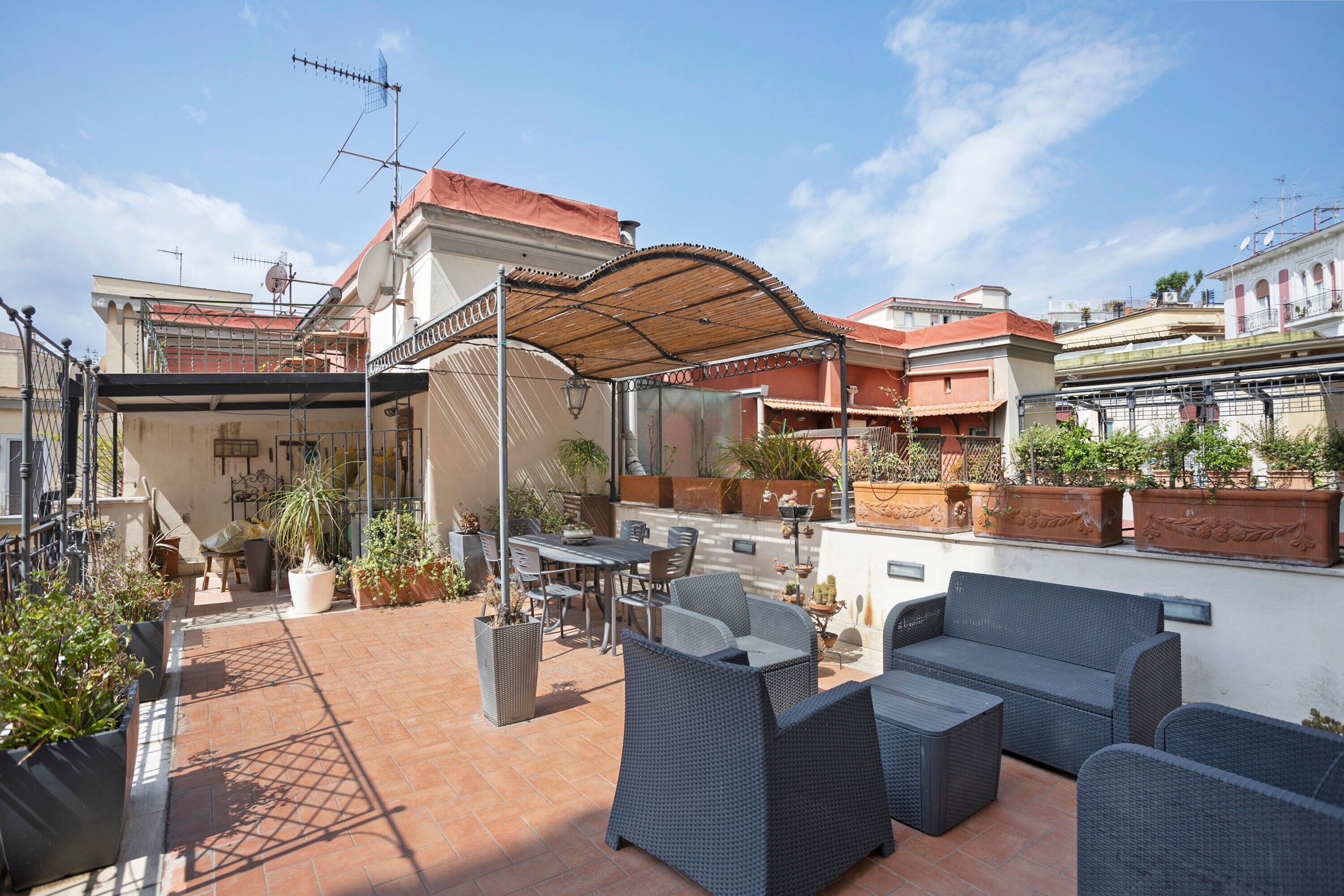 Eine Dachterrasse mit Gartenmöbeln, Topfpflanzen und einer Pergola, die Schatten spendet.