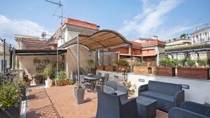 Een dakterras met buitenmeubilair, potplanten en een pergola voor schaduw.