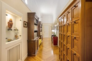 A hallway with wooden cabinets, a glass display case with decorative items, and a red planter. - La Dimora Dei Reali - Bordeaux Suite with Private Terrace (Naples)