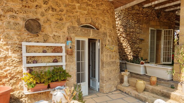A stone building with a rustic exterior, a white door, and a small garden area with potted plants and a statue. - Villa 'Tenuta Rosa in Salento' with Private Terrace, Private Garden and Air Conditioning (Taviano)