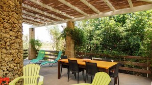 An outdoor patio with a stone wall, wooden pergola, and a table with chairs. - Villa 'Tenuta Rosa in Salento' with Private Terrace, Private Garden and Air Conditioning (Taviano)