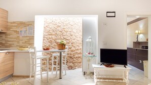 A modern kitchen with a dining area, a stone wall, and a TV in a living space. - Villa 'Tenuta Rosa in Salento' with Private Terrace, Private Garden and Air Conditioning (Taviano)